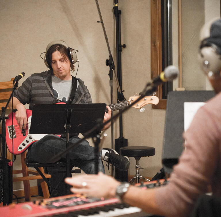 A man playing a red bass guitar in a recording studio.